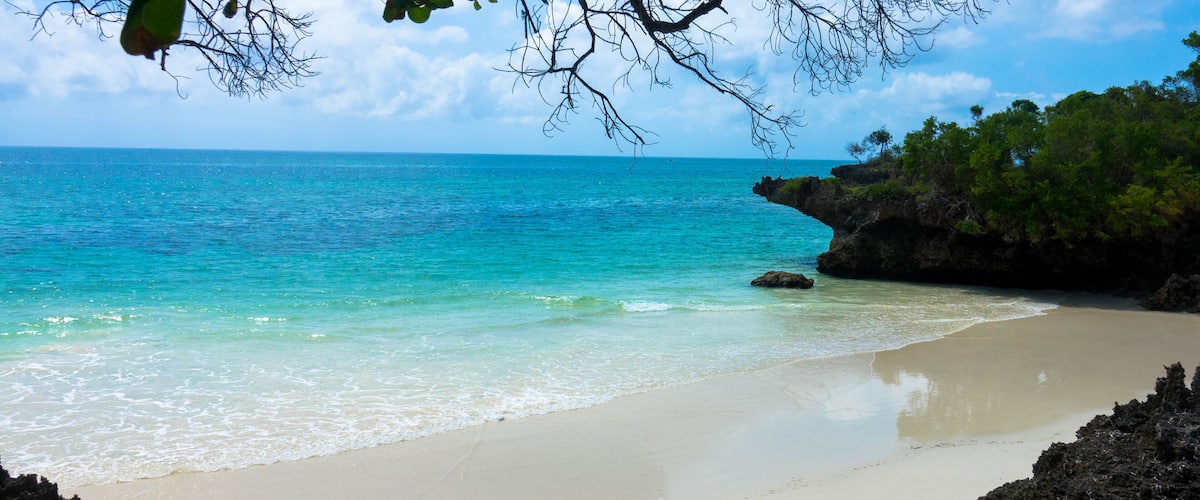 A beach with clear turquoise water, a sandy shore, and rocky outcrops.