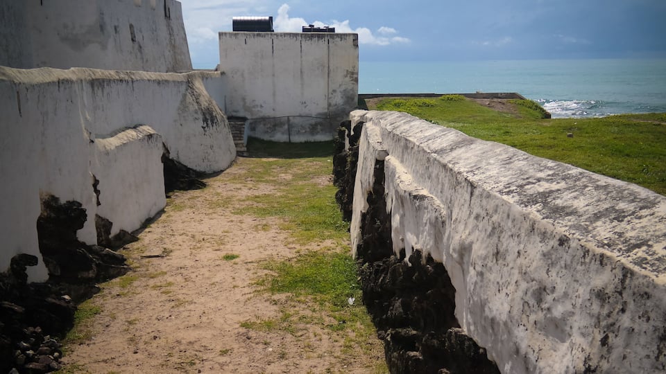 A coastal fortification with a dirt path leading to a grassy area overlooking the sea.