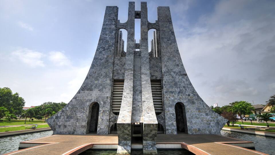 A large stone monument with a central vertical structure and two side wings, situated by a body of water.