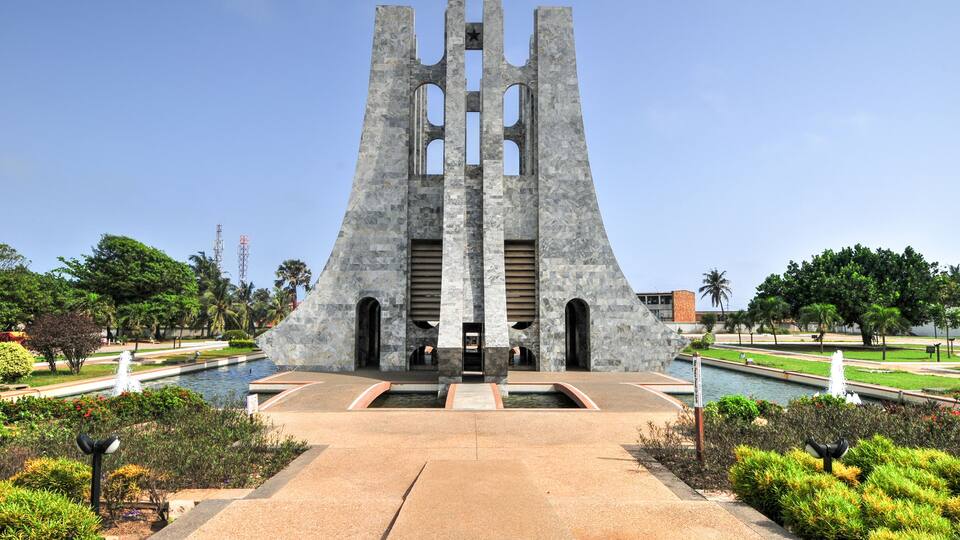 A large stone monument with a star on top, surrounded by a landscaped garden with a pond and fountains.