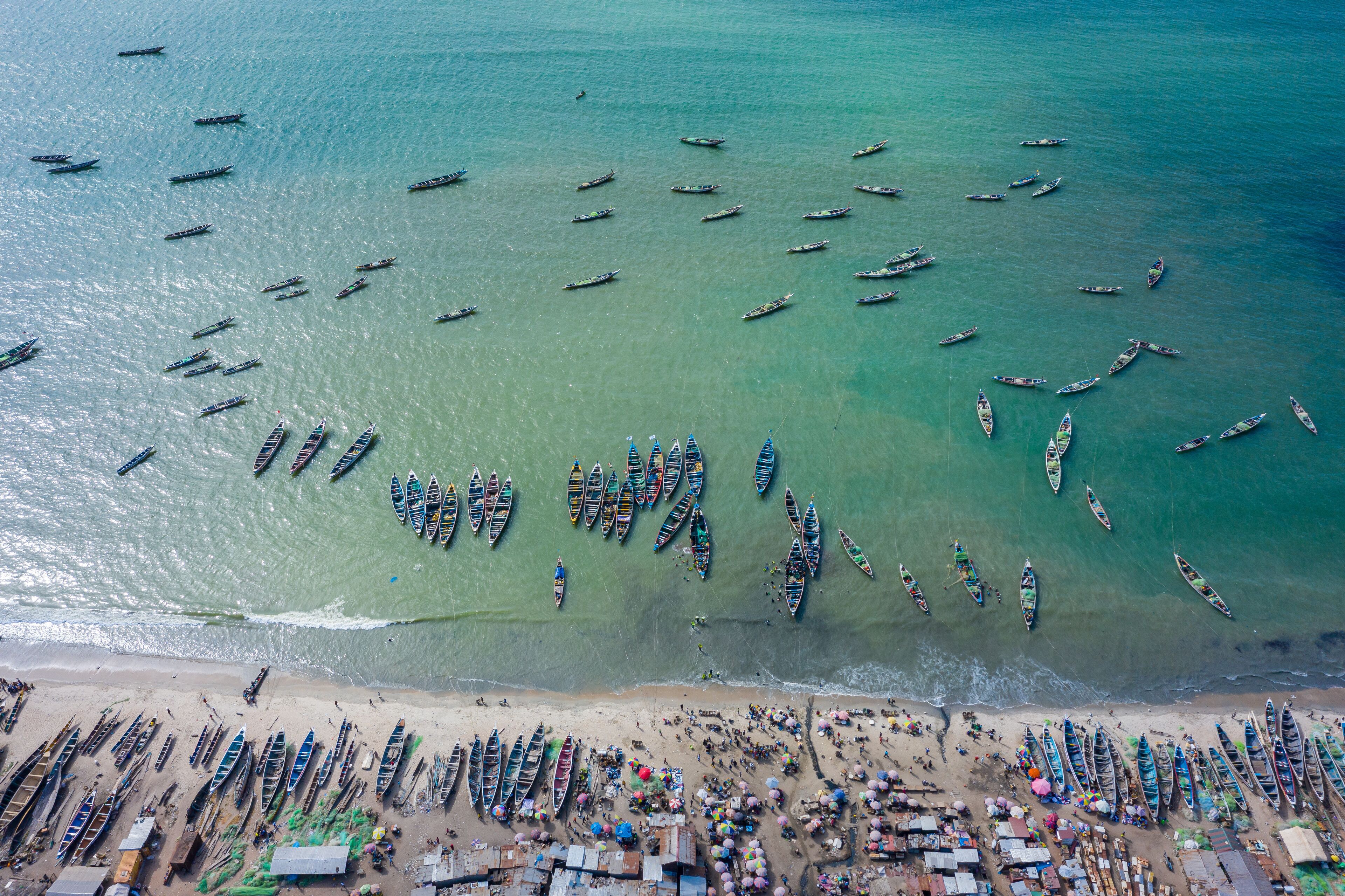 A beach with numerous boats lined up along the shore and a large group of people gathered in the water.