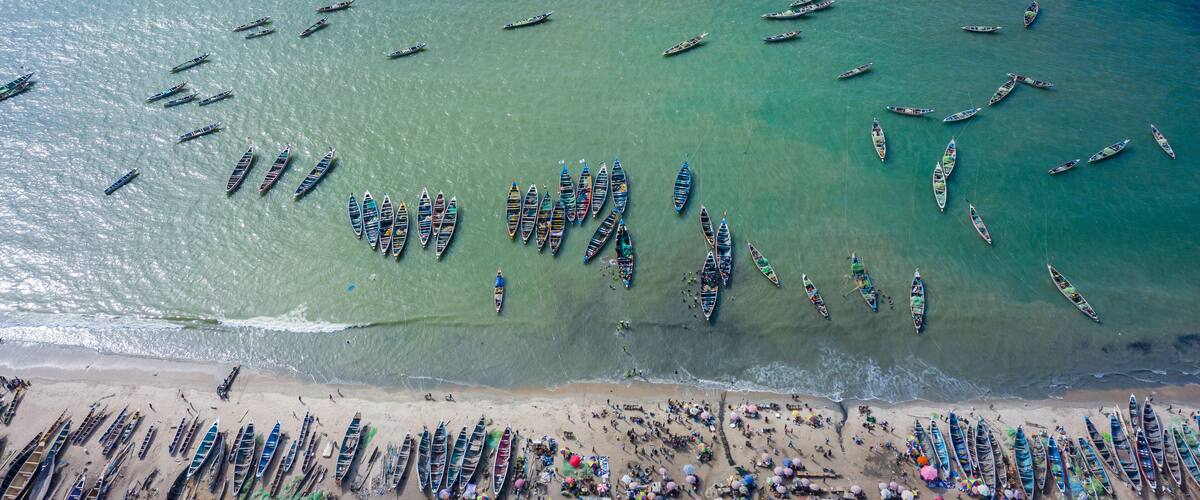 A beach with numerous boats lined up along the shore and a large group of people gathered in the water.