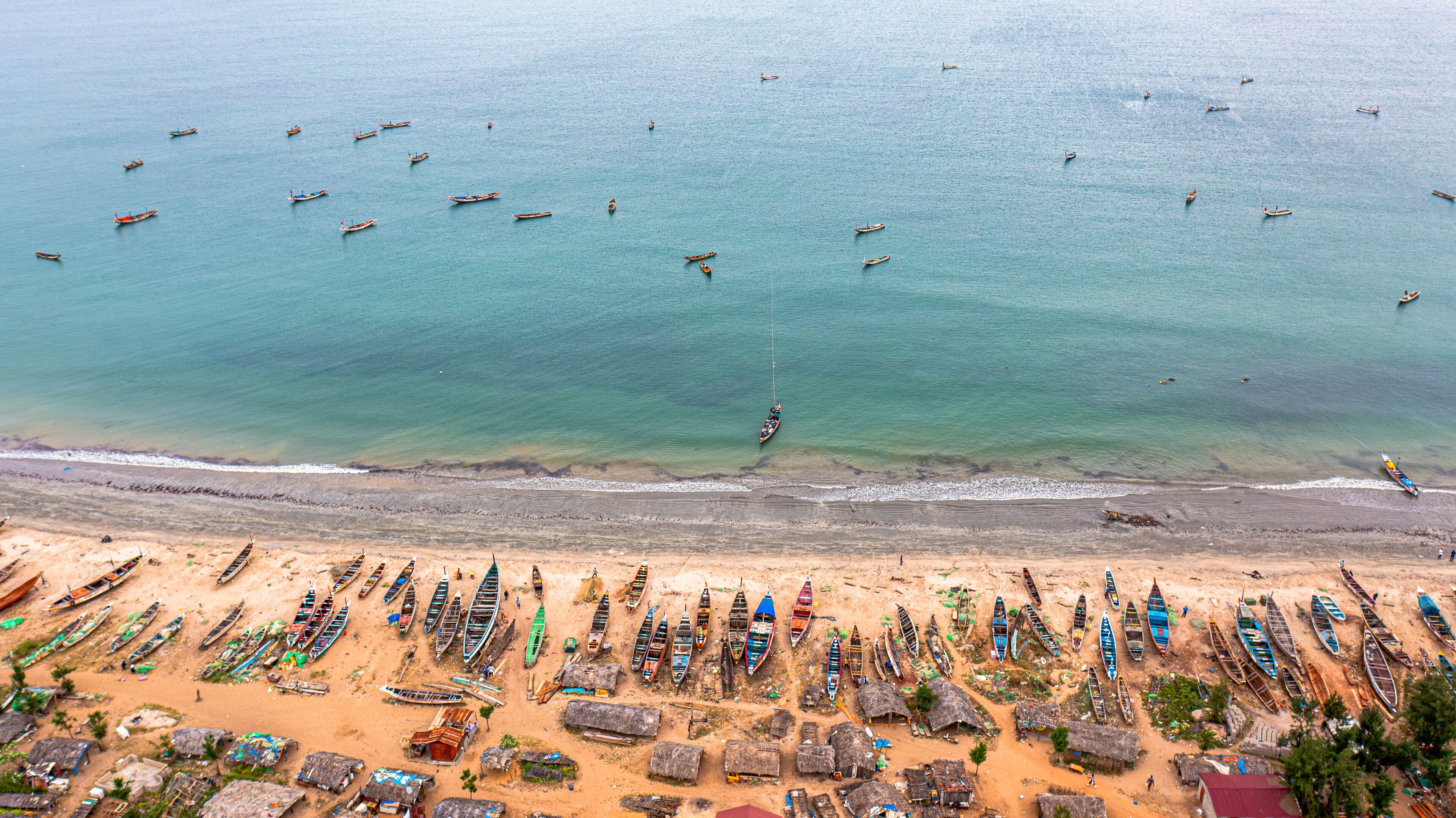 A beach with numerous boats lined up along the shore and a vast expanse of calm sea.