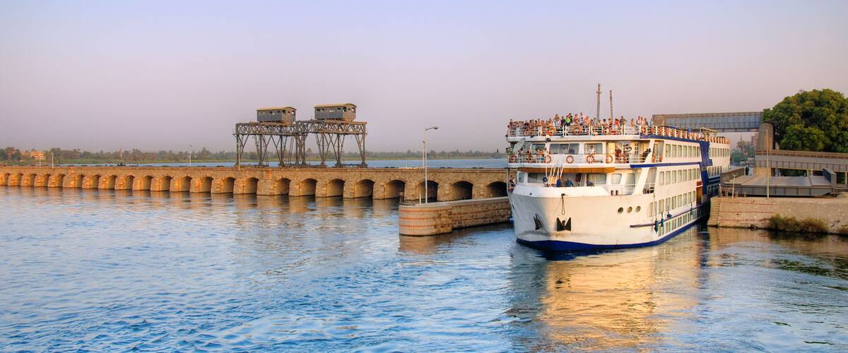 A riverboat docked at a bridge with a pedestrian walkway.