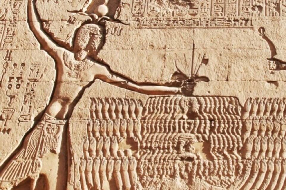 En detaljerad, forntida egyptisk relief med en central figur som håller i en stav, omgiven av hieroglyfer och en stor kobra.