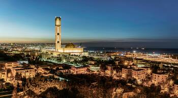 A cityscape at dusk with a prominent tower and a large dome structure.