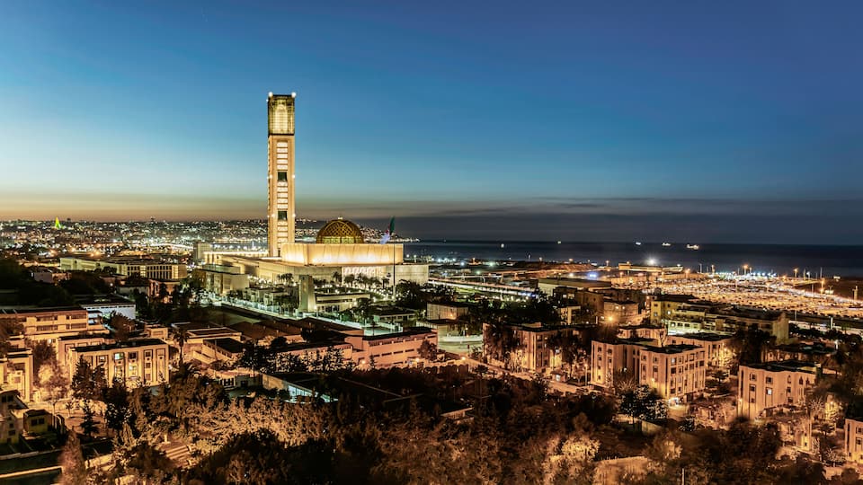 A cityscape at dusk with a prominent tower and a large dome structure.