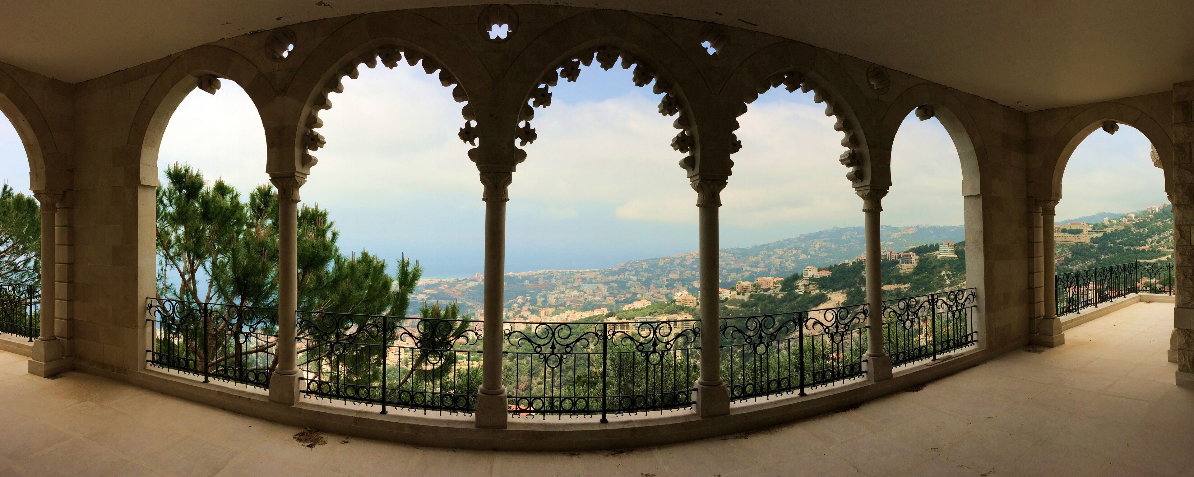 A covered balcony with stone arches and a view of a cityscape.