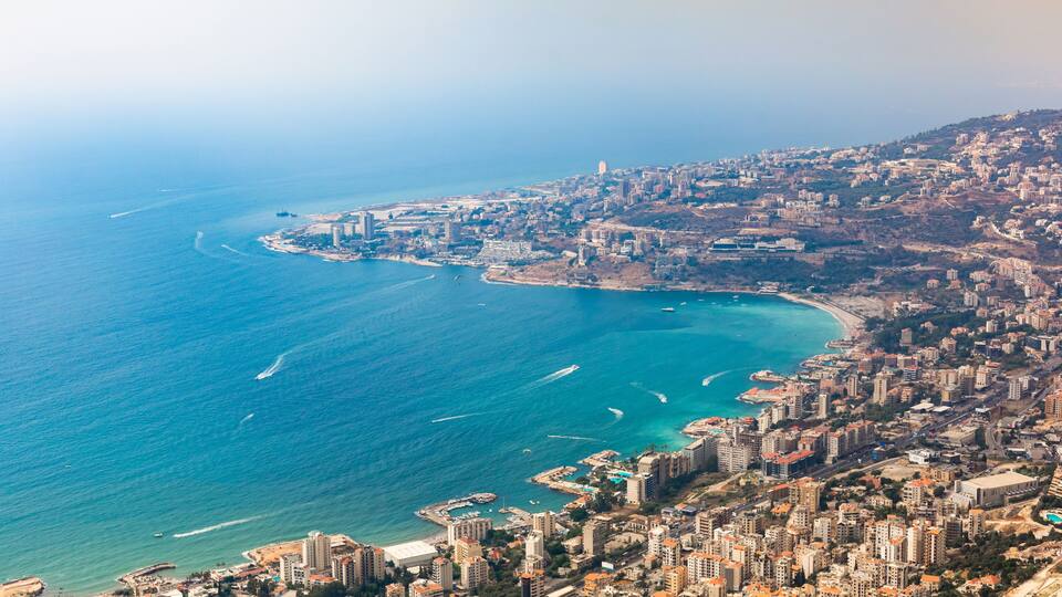 A coastal cityscape with a prominent beach, dense urban buildings, and a clear blue sea.