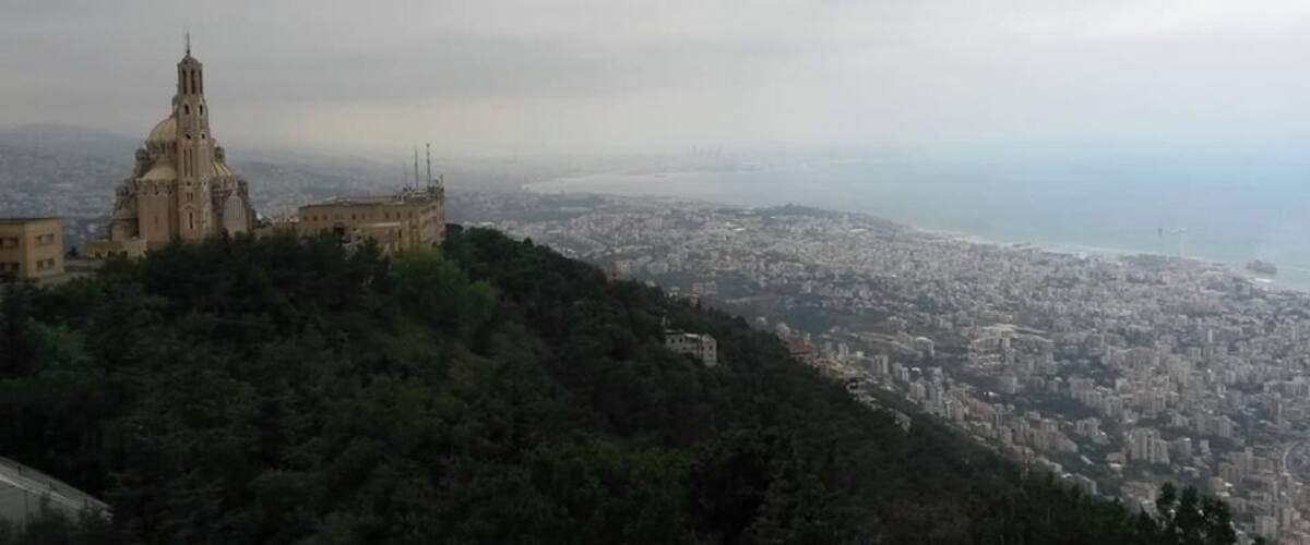 A cityscape with a prominent church on a hill and a view of the coastline.