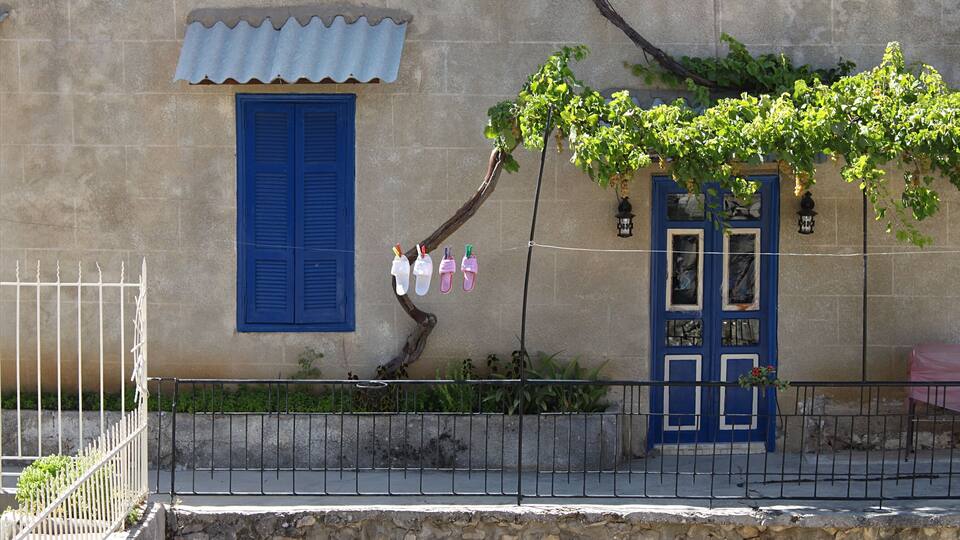 A stone building with blue shutters, a metal fence, and a tree with green leaves.