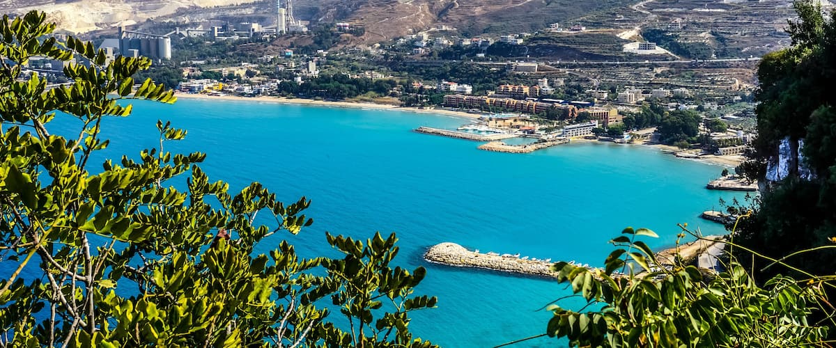 A coastal city with a clear blue sea, green hills, and buildings.