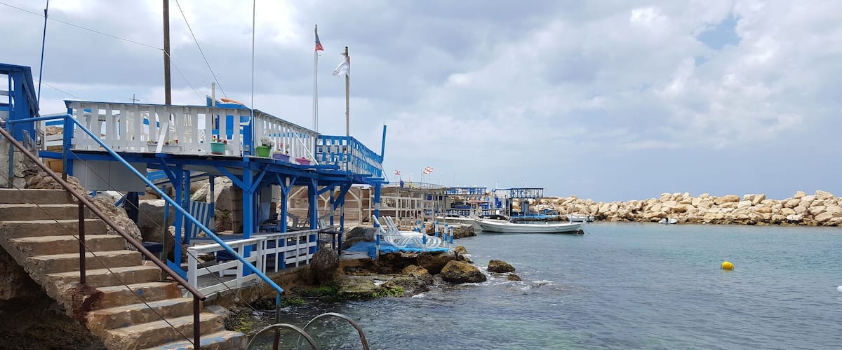 A coastal pier with blue railings, a staircase leading down to the water, and a rocky shoreline.