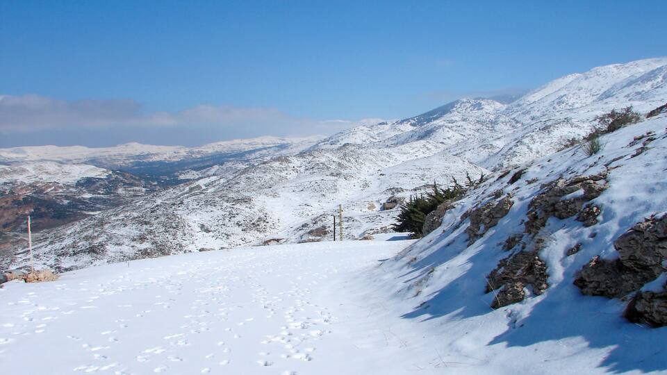 A snow-covered mountain landscape with rocky outcrops and a clear blue sky.