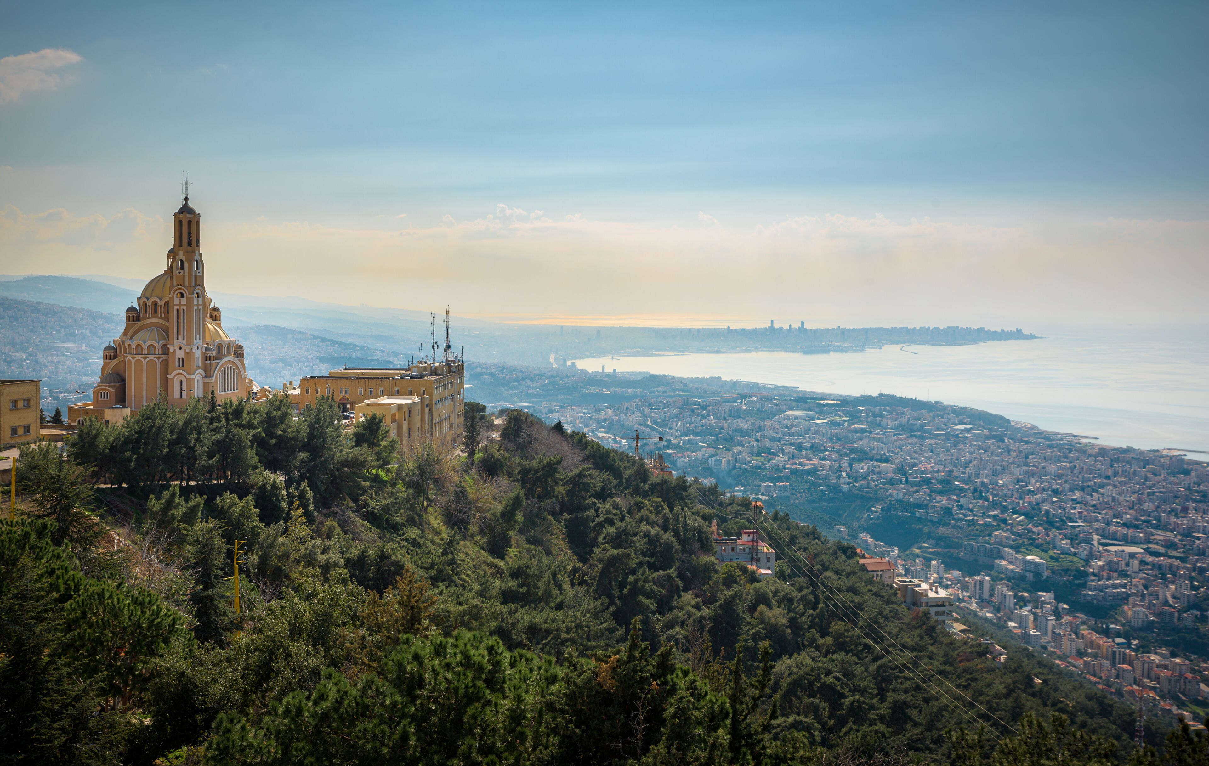 A coastal cityscape with a prominent church on a hill, dense urban area, and a body of water in the distance.