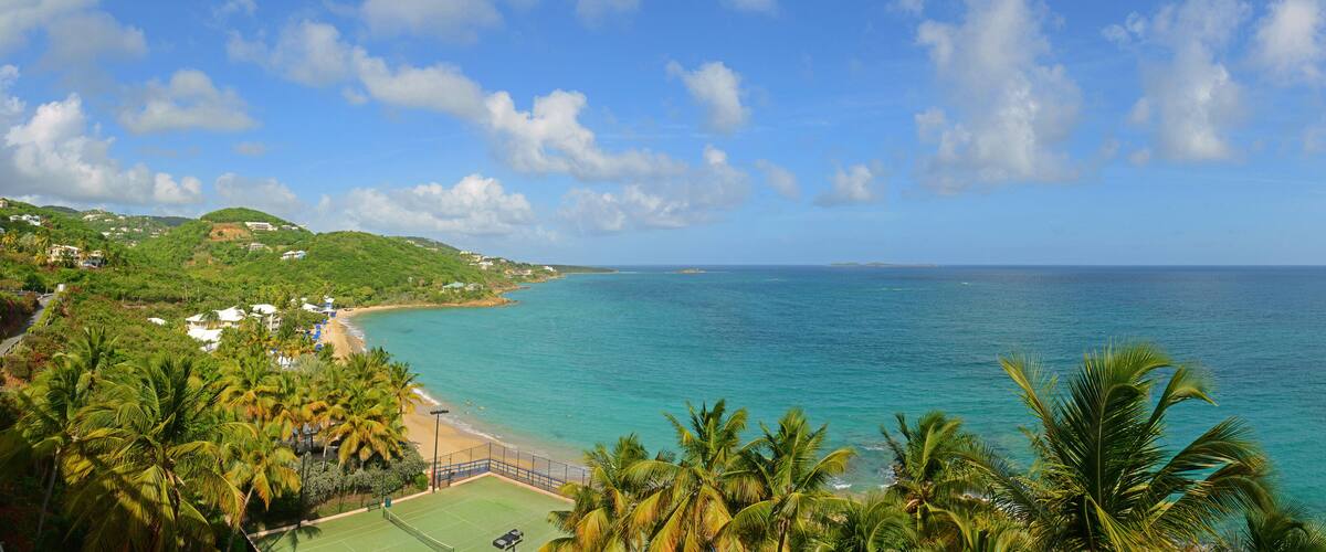 A coastal landscape with a beach, palm trees, and a tennis court.