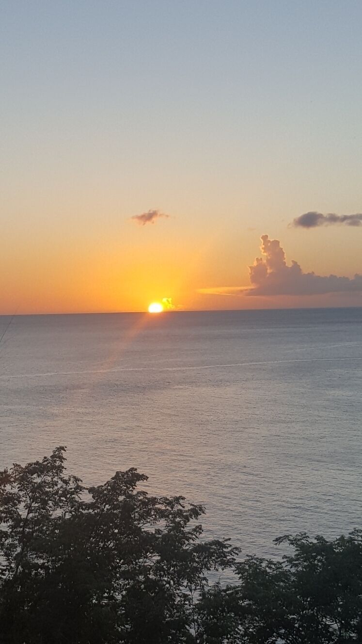 A sunset over a calm sea with a few clouds in the sky.