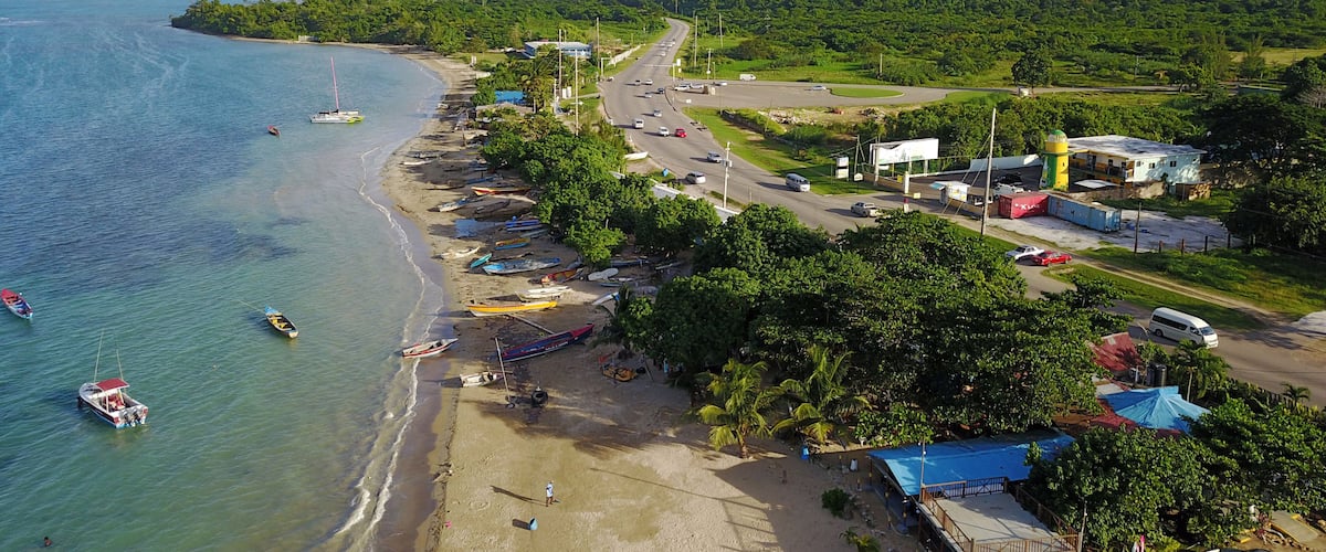 A coastal town with a beach, boats, and a road leading to a hill.