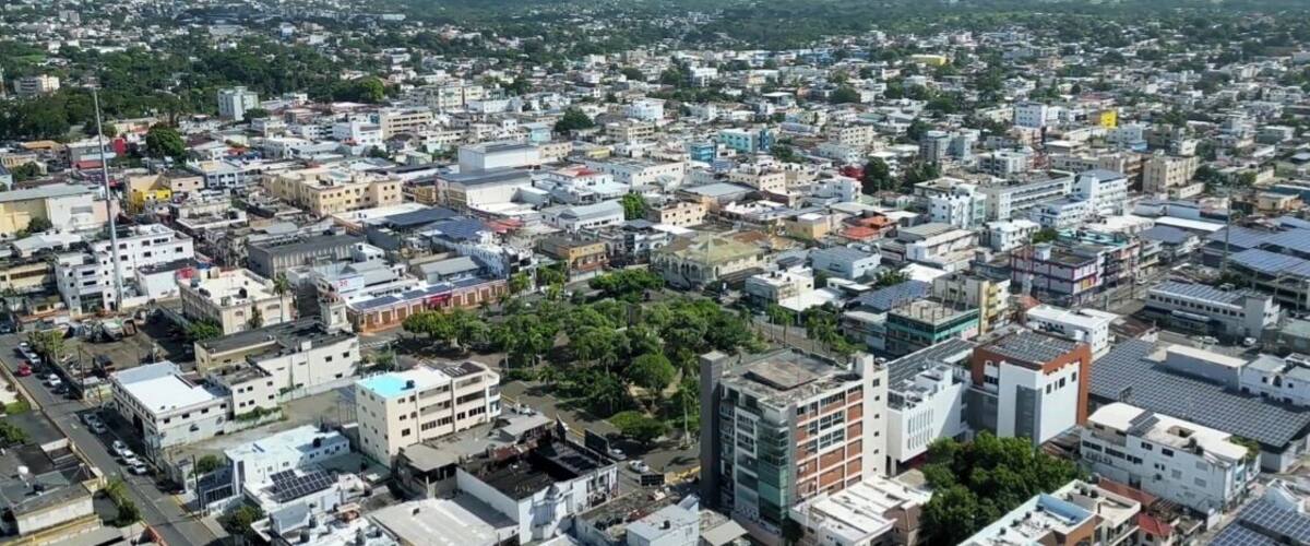 A densely populated urban area with a mix of residential and commercial buildings, surrounded by greenery and distant mountains.