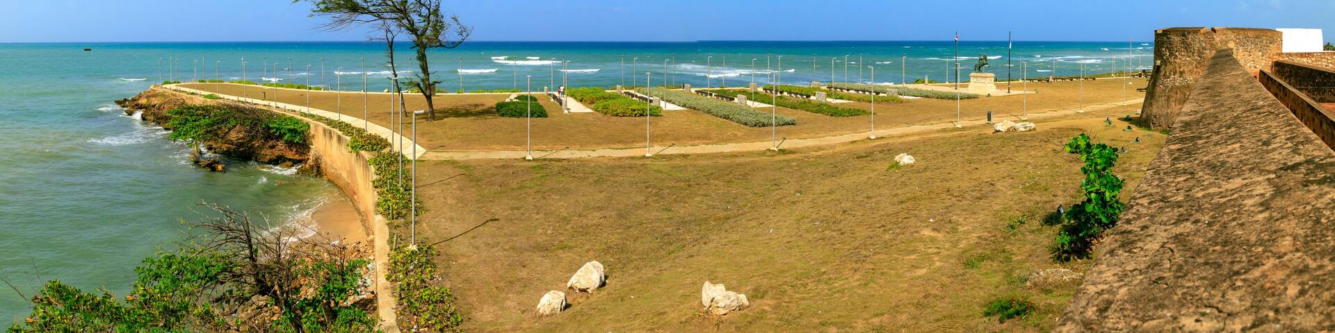 A coastal park with a walking path, a statue, and a stone wall overlooking the sea.