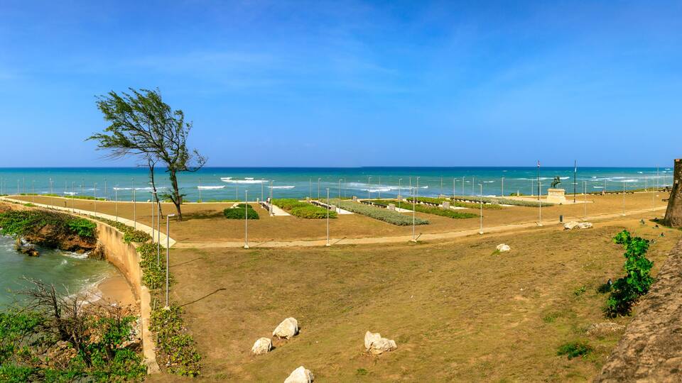 A coastal park with a walking path, a statue, and a stone wall overlooking the sea.