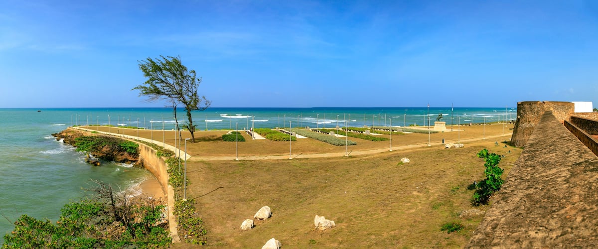 A coastal park with a walking path, a statue, and a stone wall overlooking the sea.