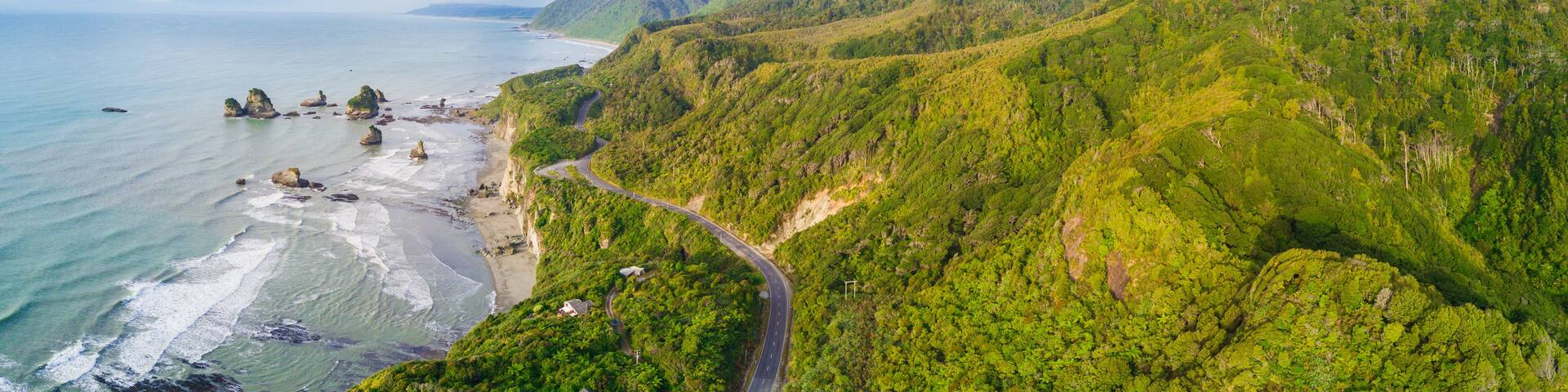A coastal landscape with a winding road, lush green hills, and rocky outcrops.