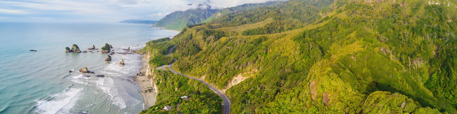 Paisagem costeira com estrada sinuosa, colinas verdes exuberantes e afloramentos rochosos.