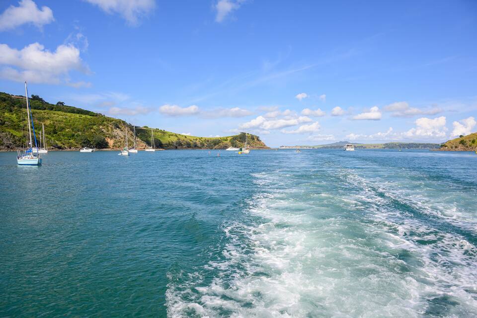 A calm sea with sailboats and a ferry.