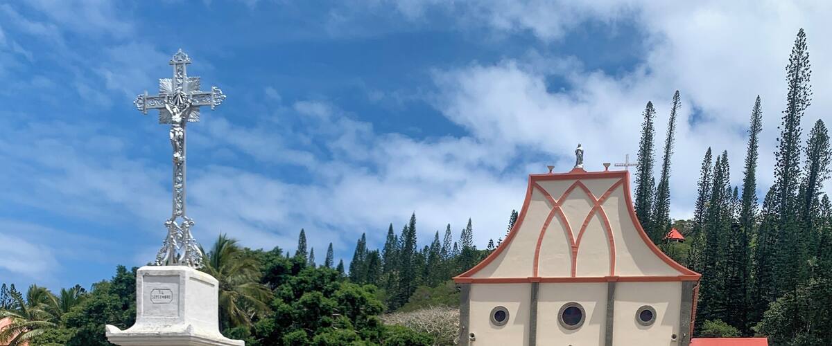 A church with a red roof and a cross monument in front.