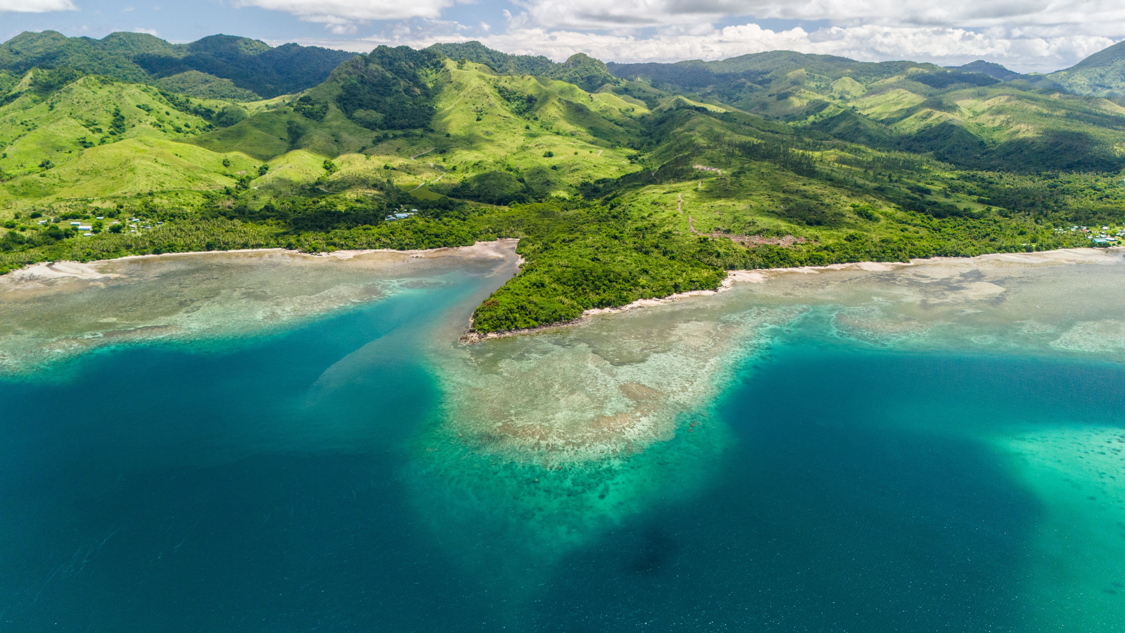 A coastal landscape with lush green hills and clear turquoise waters.