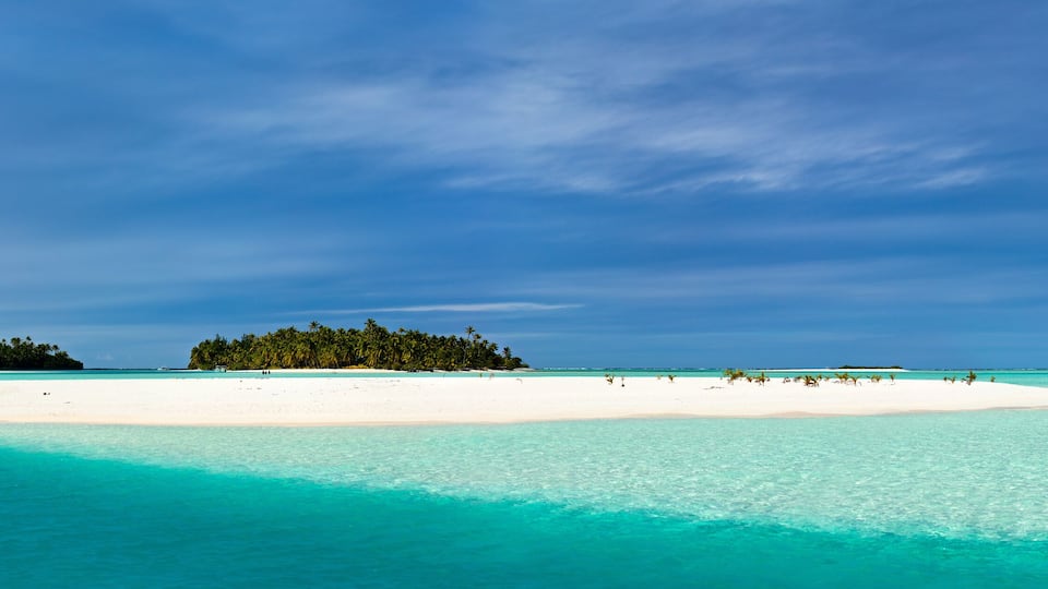 A white sandy beach with turquoise waters and a forested island in the distance.