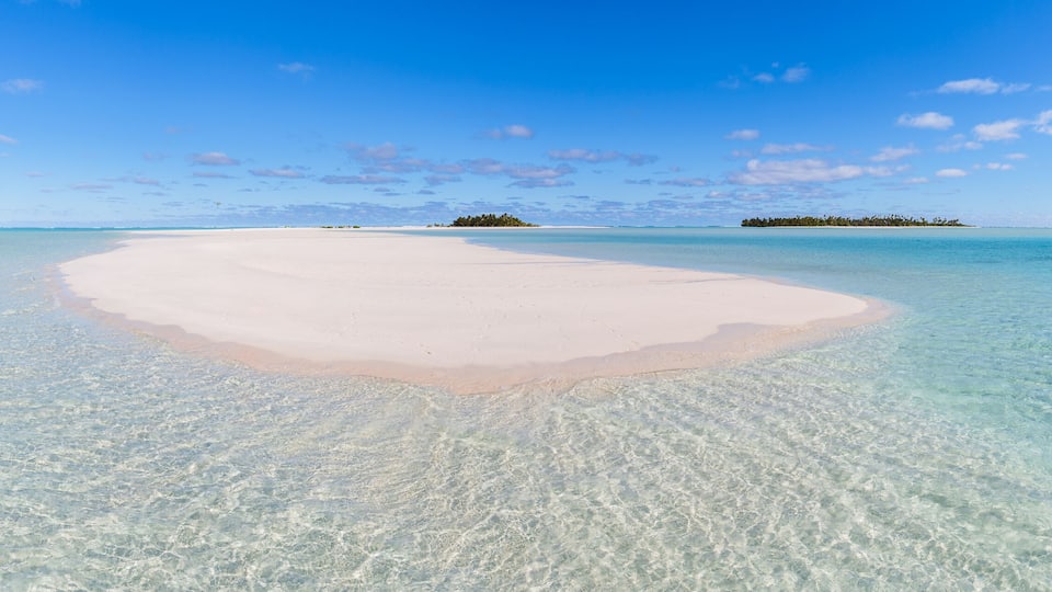 A clear turquoise sea with a white sandy beach and a small island in the distance.