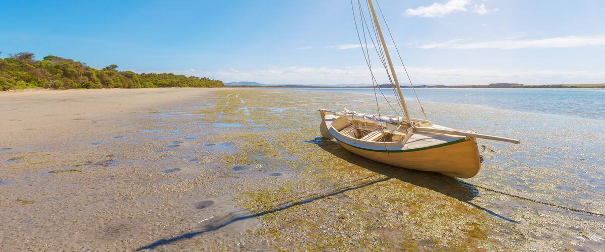 A small boat on a clear, shallow beach with calm water and a distant shoreline.