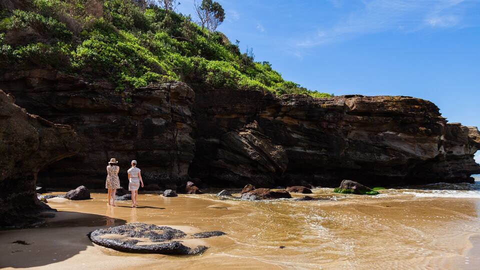 Two people walking along Aussie beach towards seaside cliff