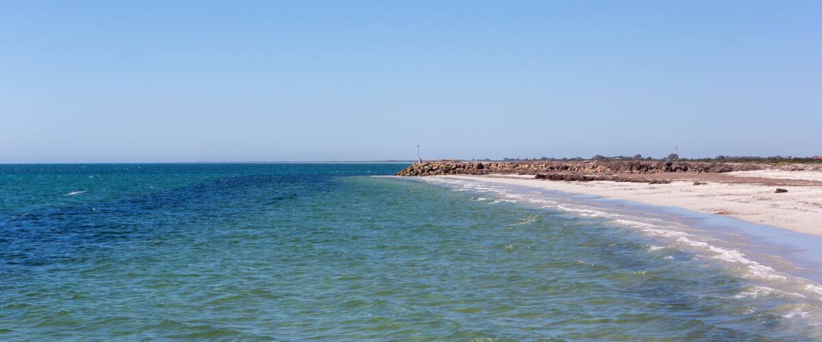 A beach with clear blue water, white sand, and rocky outcrops.