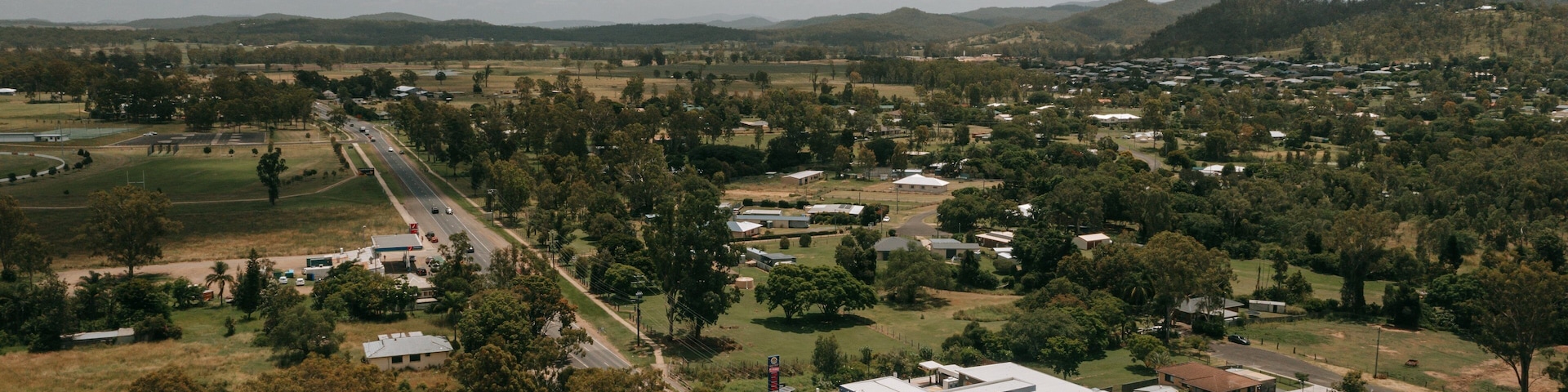 Paisaje rural con camino, edificios y colinas al fondo.