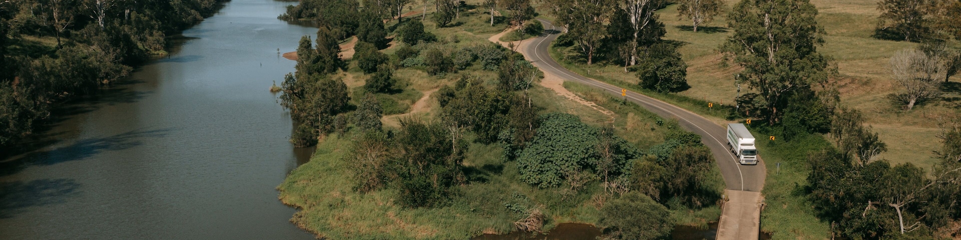 Um rio serpenteando por uma paisagem arborizada, com uma estrada sinuosa ao lado.
