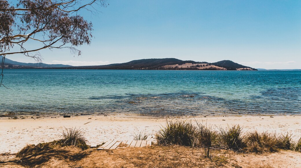 Una playa con agua cristalina, orilla de arena y colinas a lo lejos.