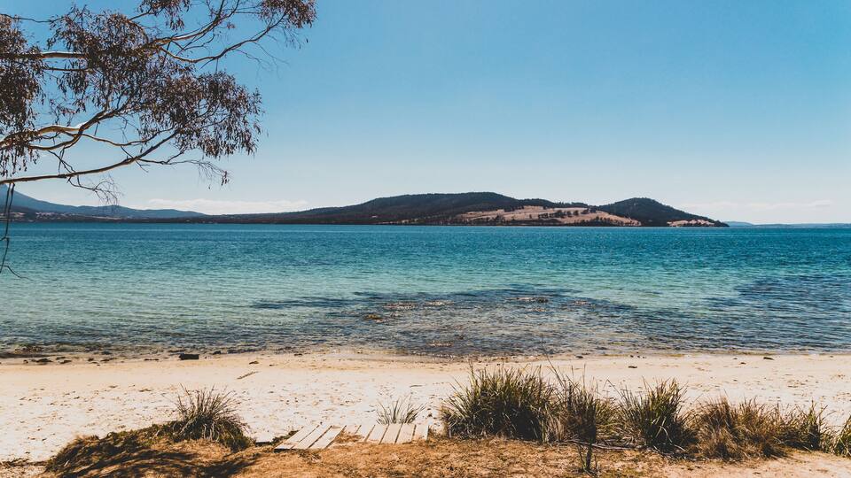 A beach with clear water, sandy shore, and distant hills.