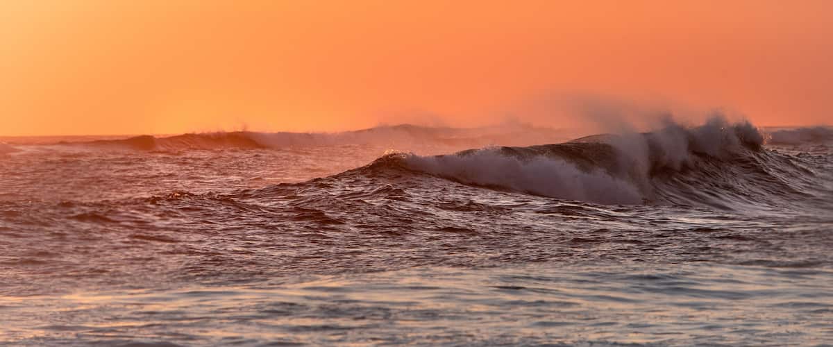 A sunset over the ocean with waves crashing onto the shore.
