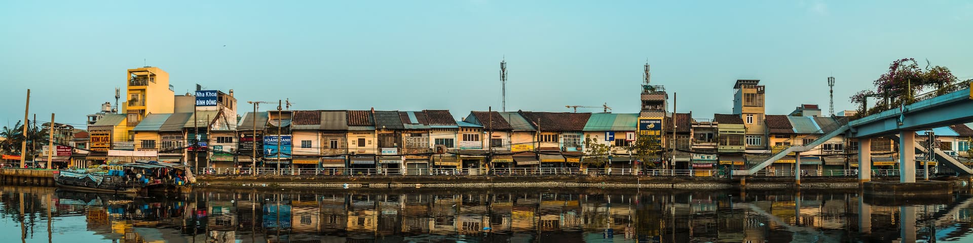 A riverside cityscape with buildings reflecting on the water, a bridge, and a tower.