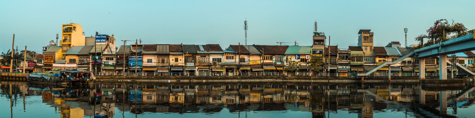 Un paisaje urbano a la orilla del río, con edificios reflejados en el agua, un puente y una torre.