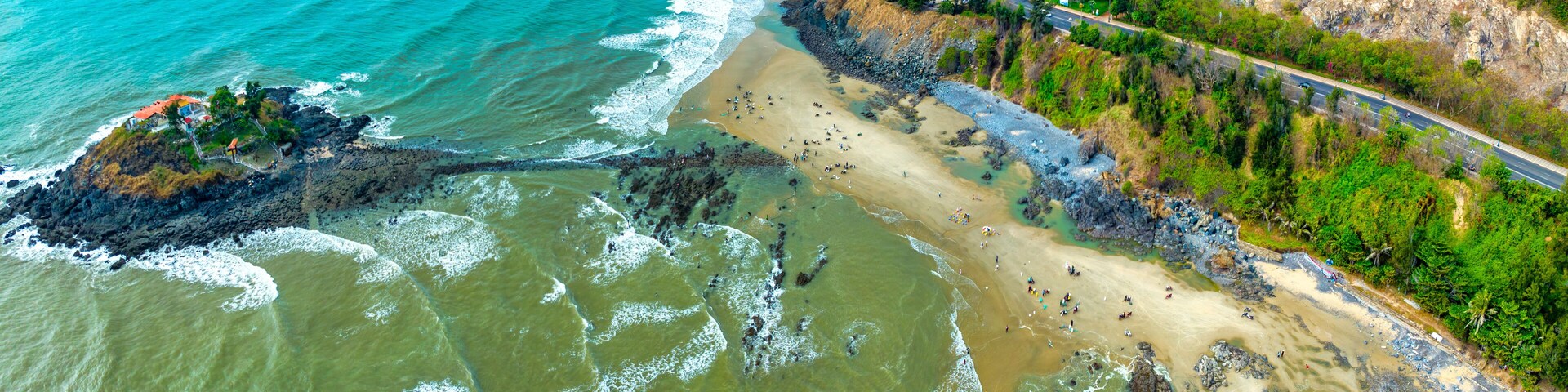 Paisaje costero con playa, acantilados rocosos y un camino sinuoso.