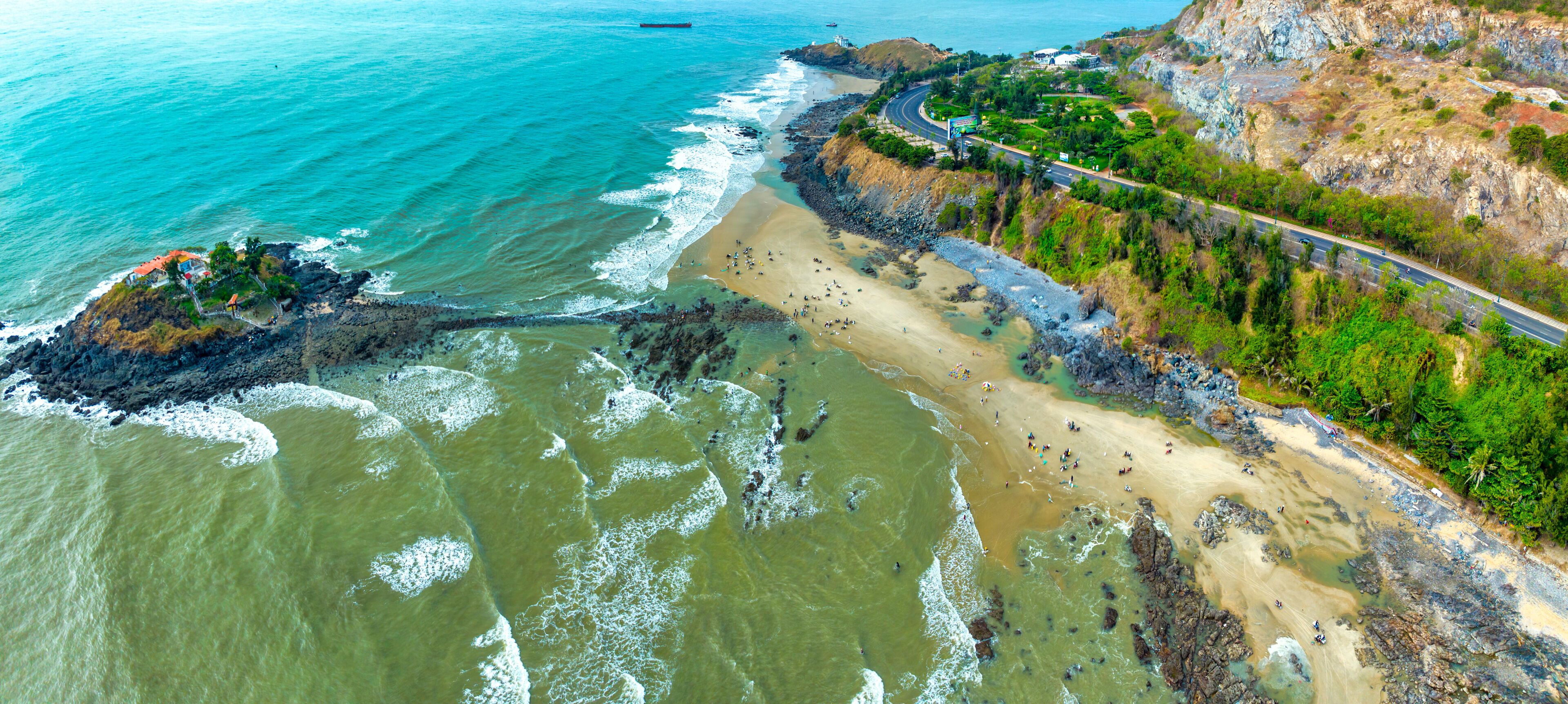 A coastal landscape with a beach, rocky cliffs, and a winding road.