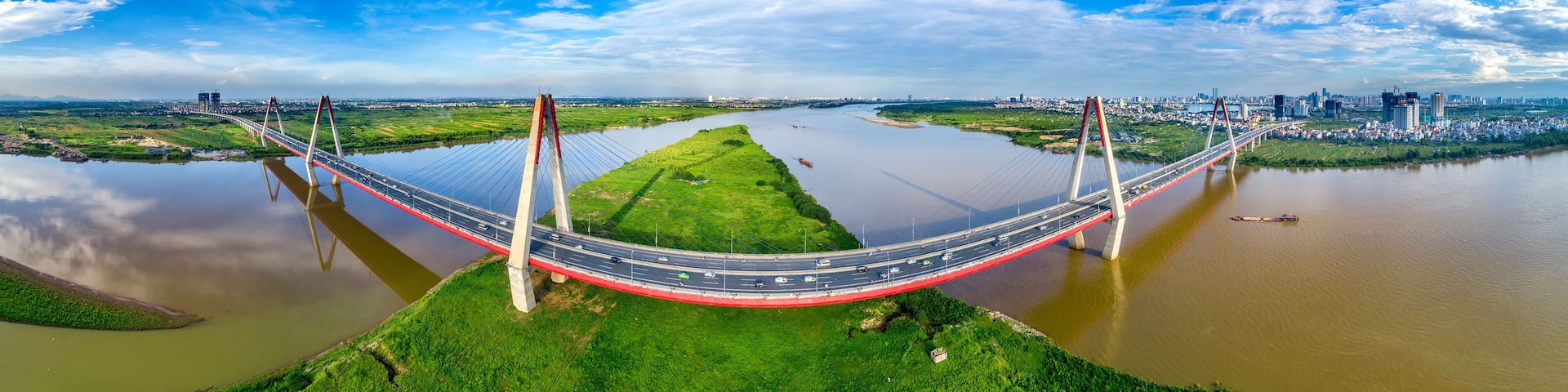 A large suspension bridge over a river with a cityscape in the background.