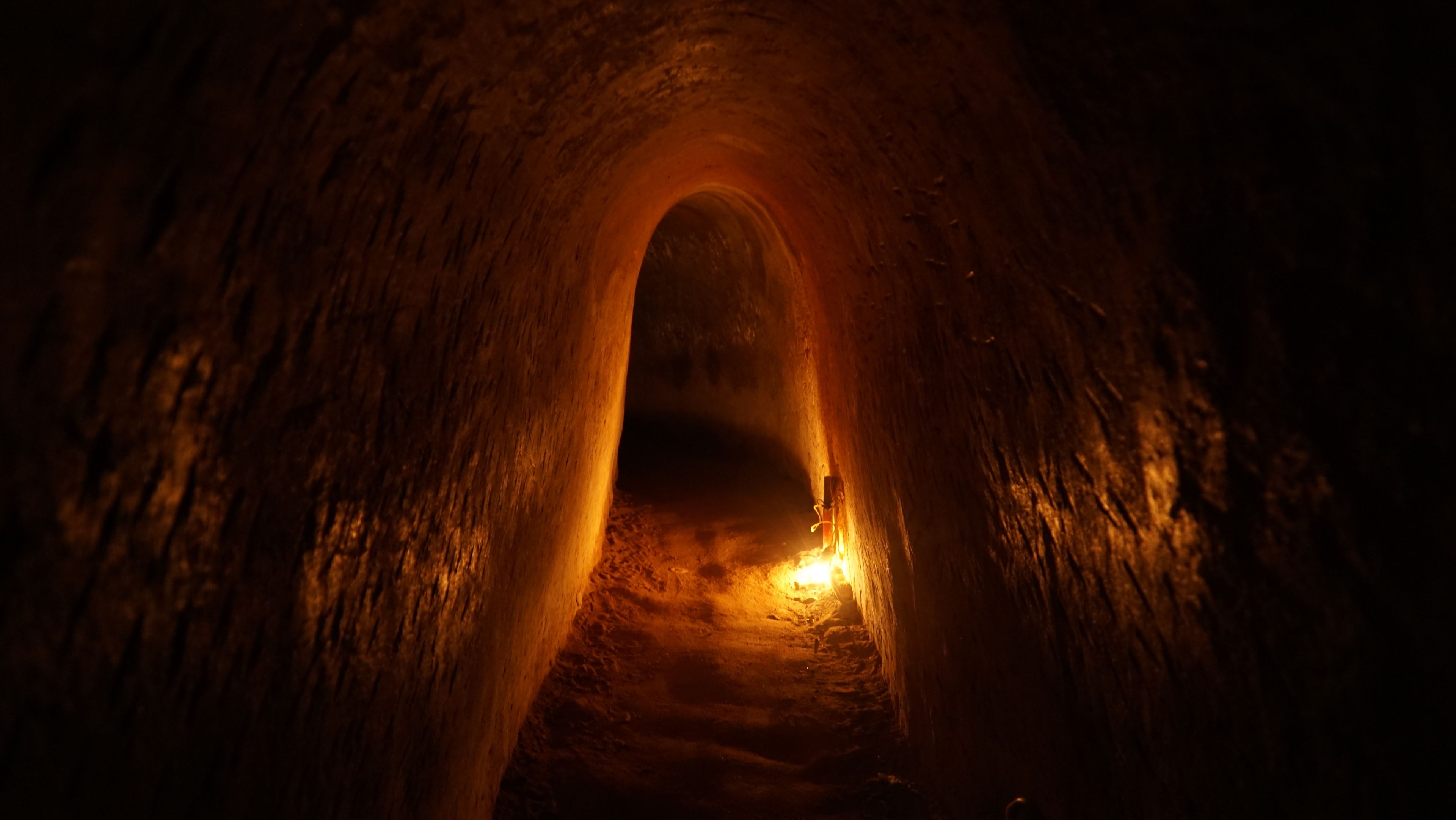 A tunnel with rough, textured walls and a warm light at the end.