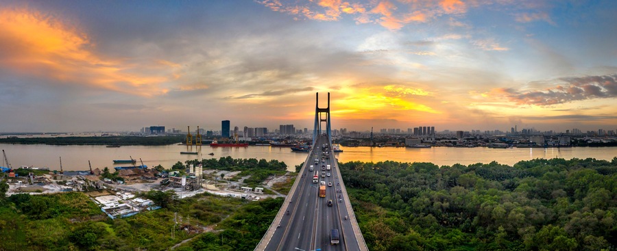 A bridge with a city skyline in the background, a river, and a sunset.