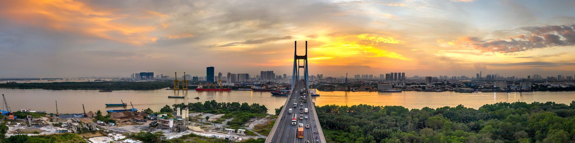 Uma ponte com um horizonte urbano ao fundo, um rio e um pôr do sol.