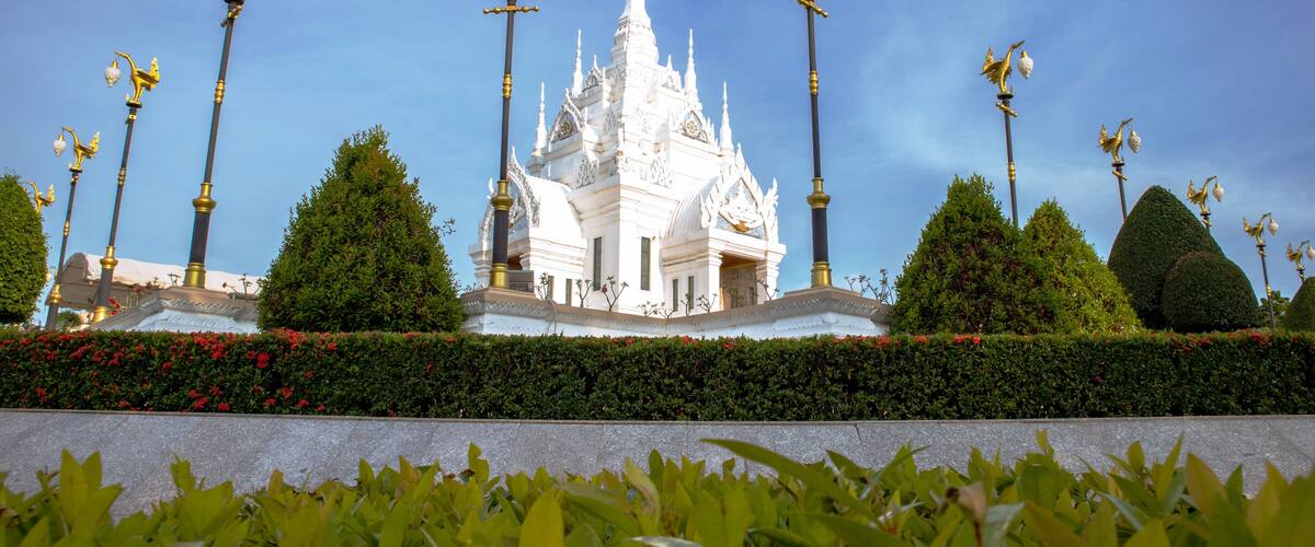 A white temple with golden statues, surrounded by neatly trimmed hedges and red flowers.